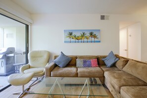 Ein Wohnzimmer mit einem Glastisch, einem beigefarbenen Sofa und einem Bild von Palmen.