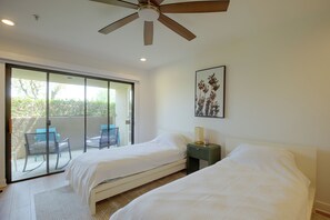 Ein Schlafzimmer mit zwei Betten, einem Deckenventilator, einem Fenster mit Blick auf Grünflächen und einem gerahmten Bild an der Wand.