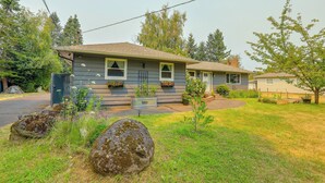 A single-story house with a front porch, a small garden with various plants, and a large rock in the foreground. - The Habitat House: Retreat by Edgefield! (Troutdale)