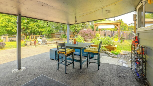 A covered patio area with a table and chairs, a garden view, and a metal rack with bags. - The Habitat House: Retreat by Edgefield! (Troutdale)