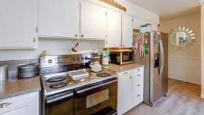 A kitchen with white cabinets, a stainless steel stove, a microwave, and a refrigerator. - The Habitat House: Retreat by Edgefield! (Troutdale)