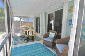 A covered patio area with a table and chairs, a wicker sofa, and a view of a backyard. - The Seaside Serenity at Thumb Point - Hutchinson Island - Prime Location - Pool Home! (Fort Pierce)