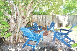 Ein Patio mit blauen Stühlen und einem Tisch, umgeben von einem Holzzaun und Bäumen.