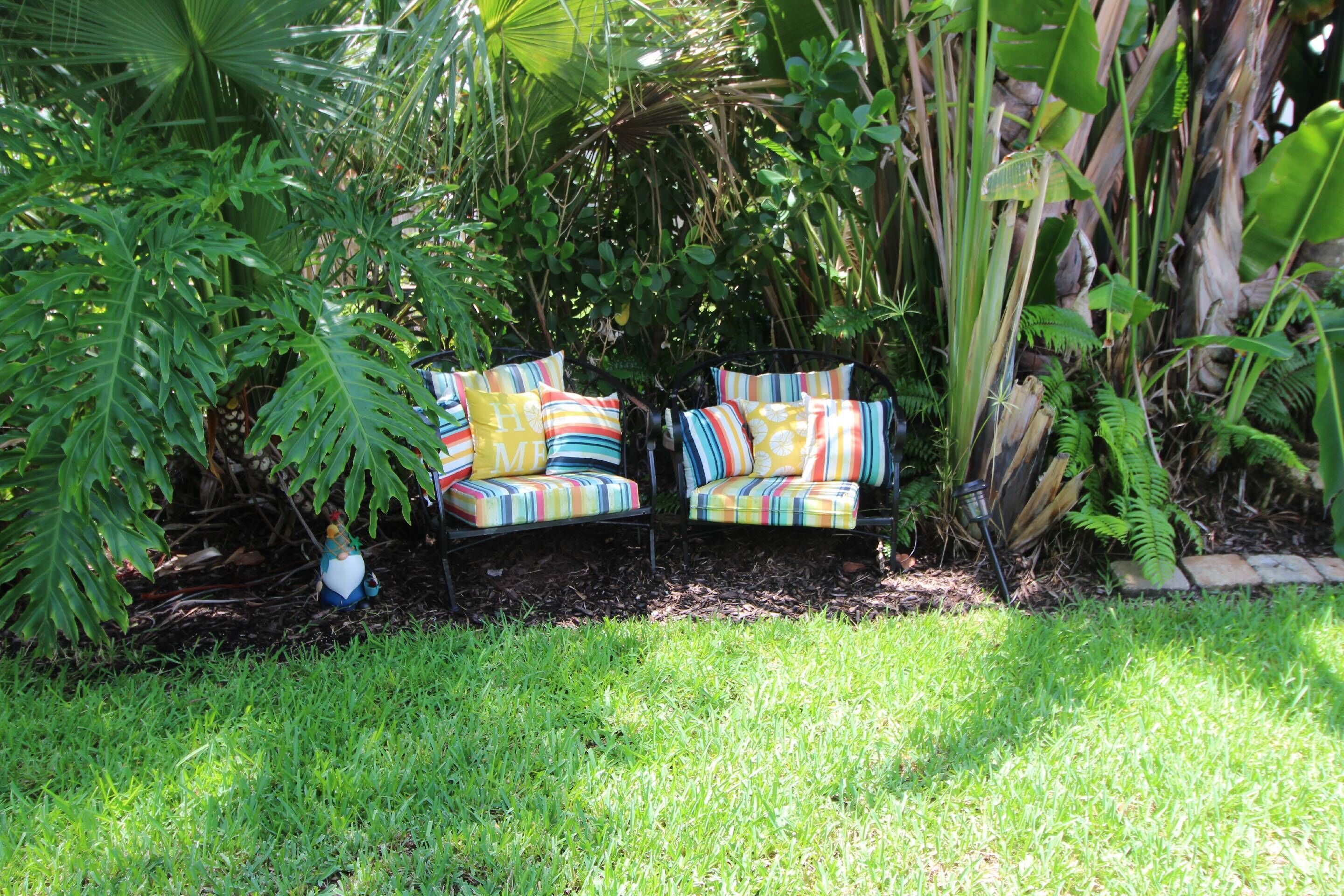 A garden with a black metal bench and colorful cushions.