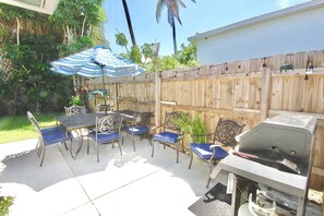Un patio al aire libre con una parrilla, una mesa y sillas, y una valla de madera.