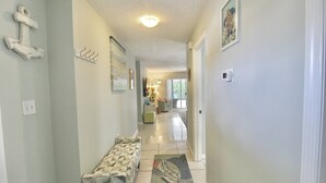 A hallway with a bench, a rug with a turtle design, a ceiling light, and a wall-mounted thermostat. - The Seaside Serenity at Thumb Point - Hutchinson Island - Prime Location - Pool Home! (Fort Pierce)