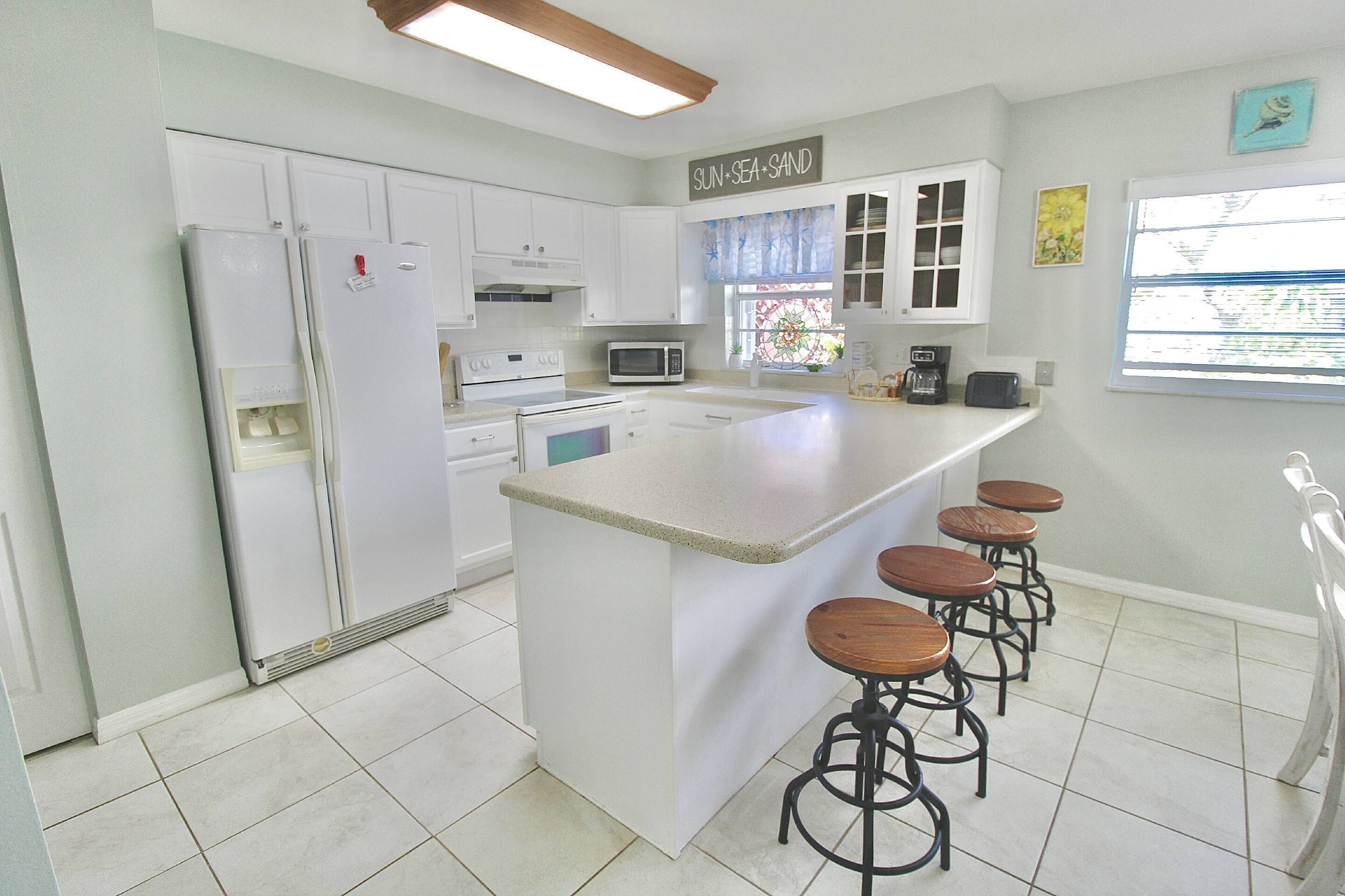 A kitchen with a central island, bar stools, a refrigerator, a microwave, and a coffee maker.