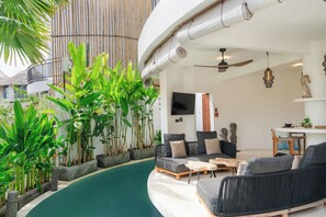 Uma sala de estar moderna com área de estar em curva, uma TV de tela plana e um ventilador de teto.