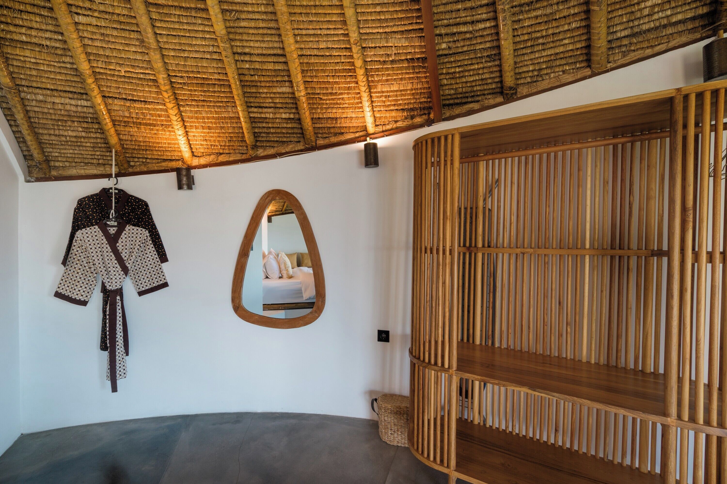 Een kamer met een gebogen plafond, een bed, een garderobe met verticale lamellen, en een spiegel aan de muur.