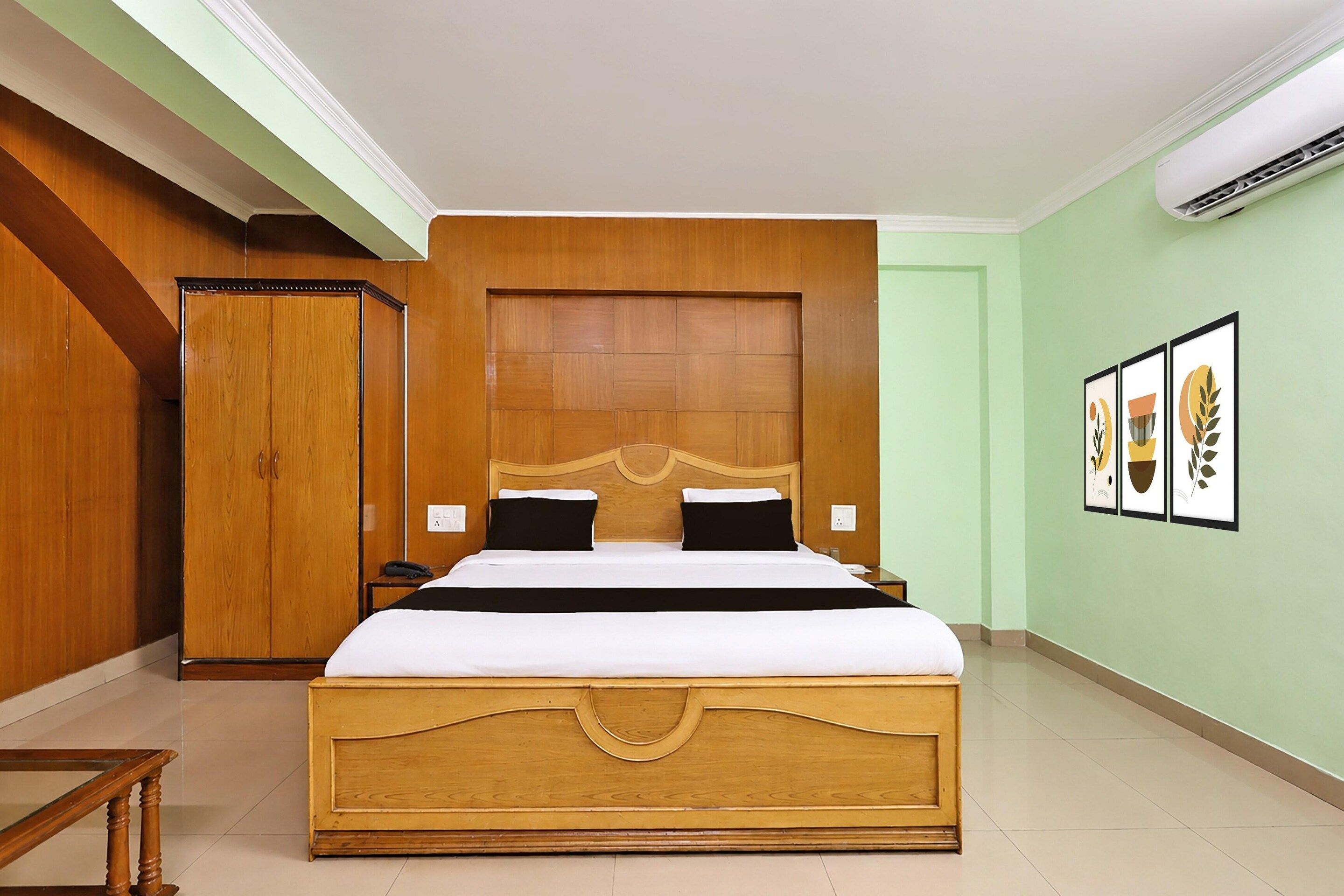 Una habitación de hotel con una cama grande, cabecera de madera, dos mesitas de noche, un armario y cuadros en la pared.