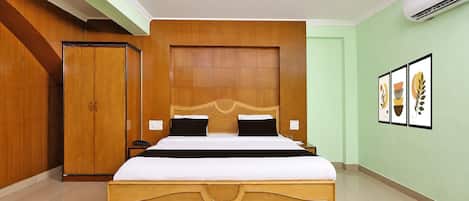 Una habitación de hotel con una cama grande, cabecera de madera, dos mesitas de noche, un armario y cuadros en la pared.