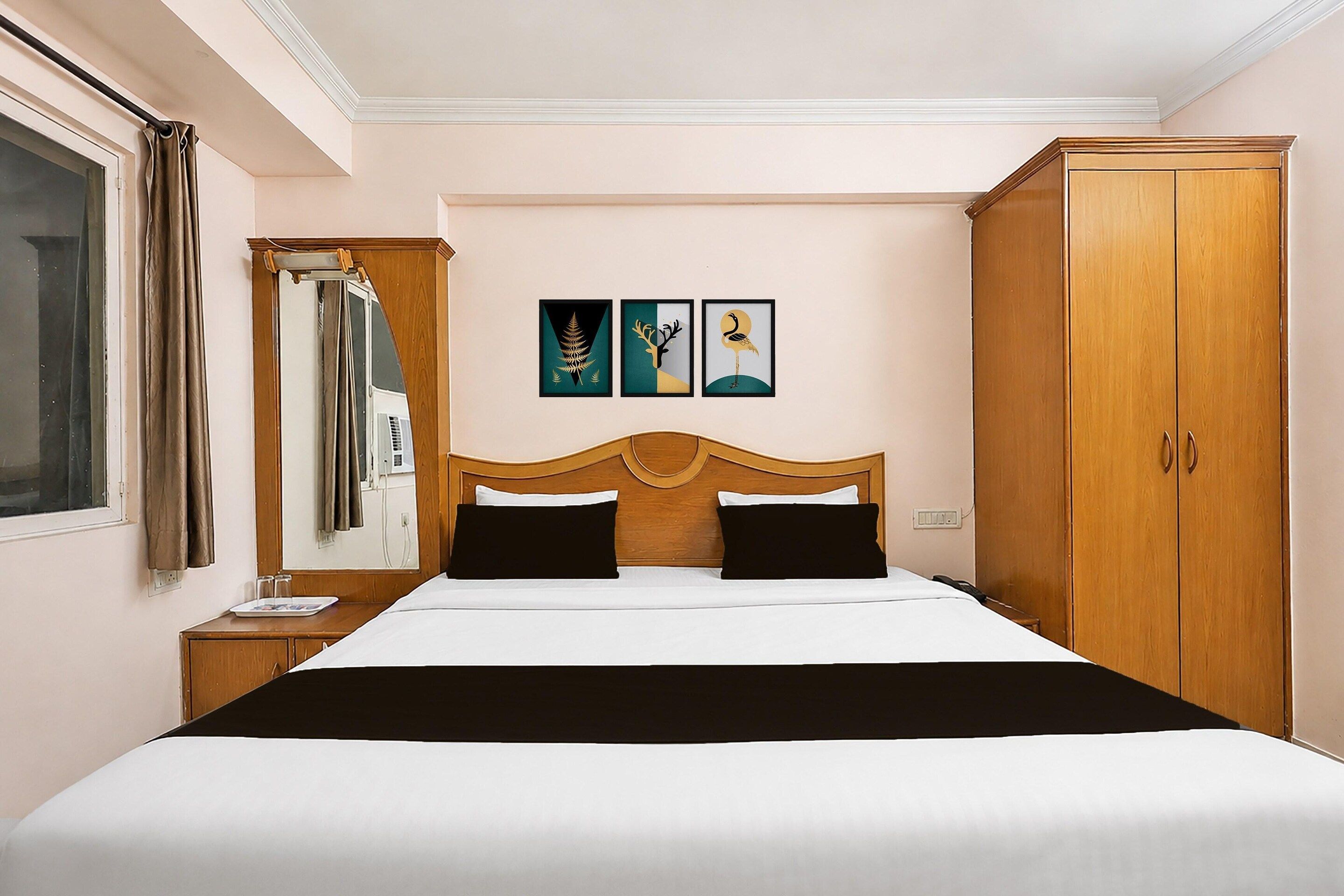 A hotel room with a large bed, a wardrobe, a mirror, and three framed pictures on the wall.