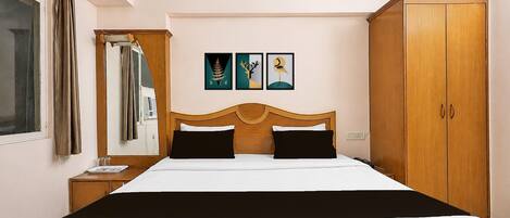 A hotel room with a large bed, a wardrobe, a mirror, and three framed pictures on the wall.
