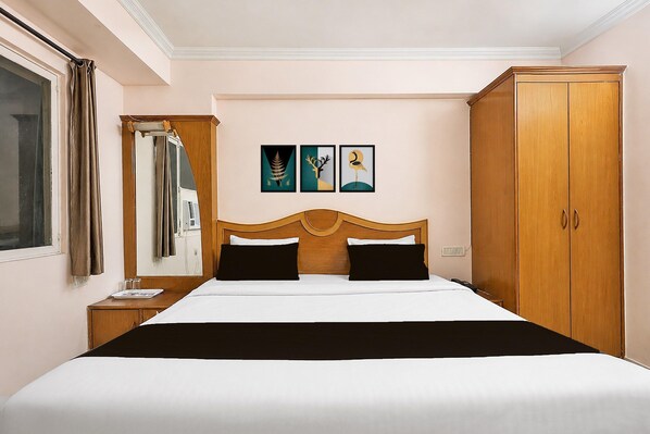 Habitación de hotel con una cama grande, un armario, un espejo y tres cuadros en la pared.