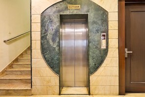 Un ascensor con un cartel arriba, un pasamanos junto a las escaleras y una puerta a la derecha.