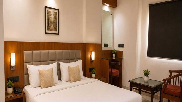 A hotel room with a large bed, bedside tables, a desk, a chair, a mirror, and a framed picture on the wall.