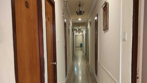 A long, narrow hallway with wooden doors on one side and a chandelier hanging from the ceiling.