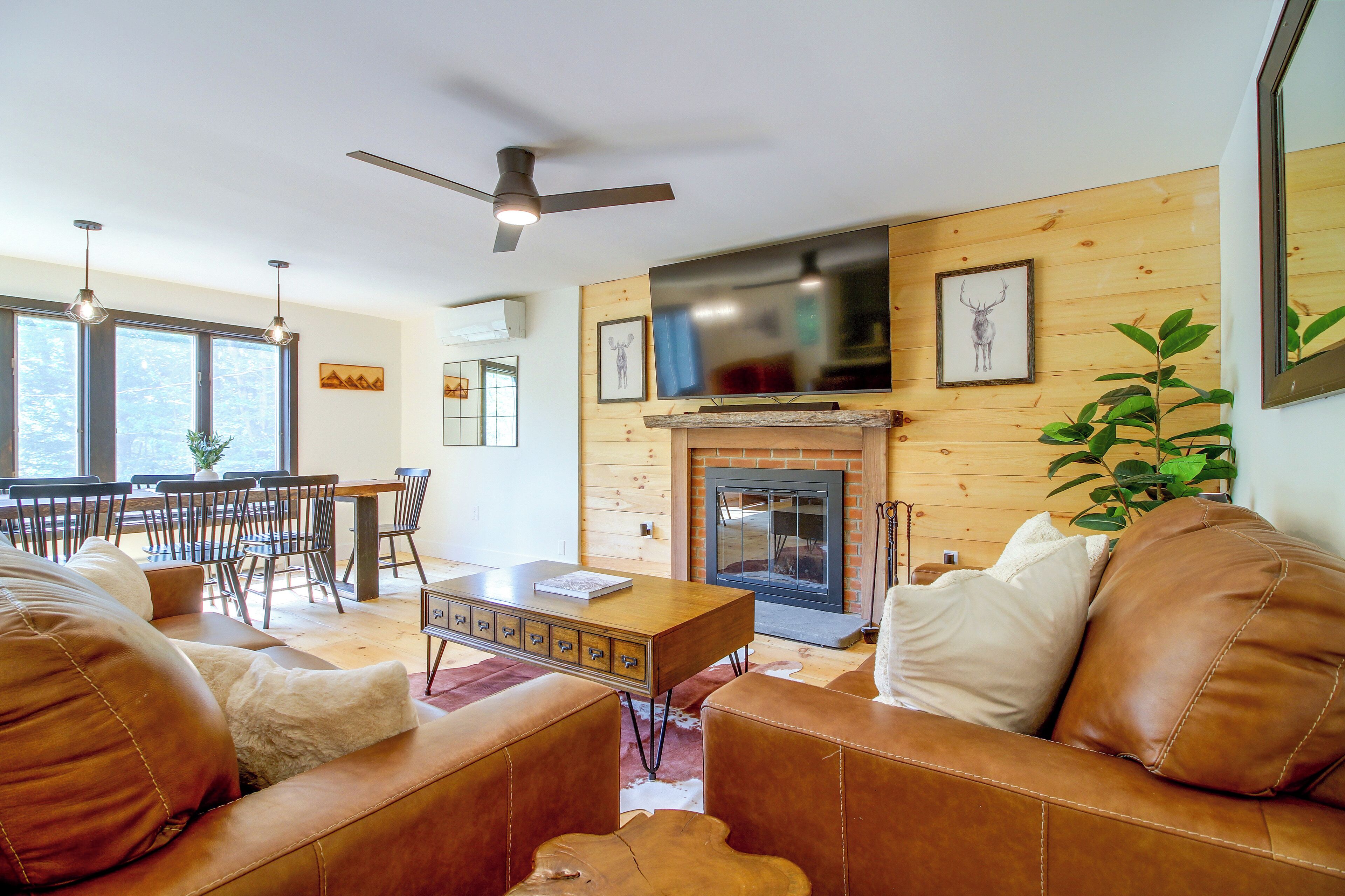 A living room with a fireplace, leather sofas, a dining area with chairs, and a television mounted above the fireplace.