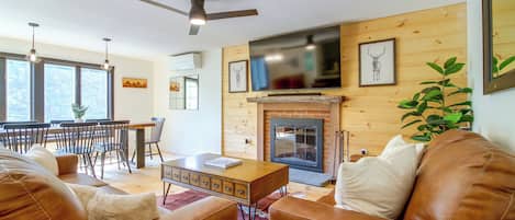 A living room with a fireplace, leather sofas, a dining area with chairs, and a television mounted above the fireplace.