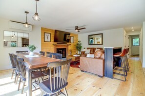 Ein geräumiges Wohnzimmer mit Holzboden, Kamin, Sofa, Fernseher und einem Esstisch mit Stühlen.