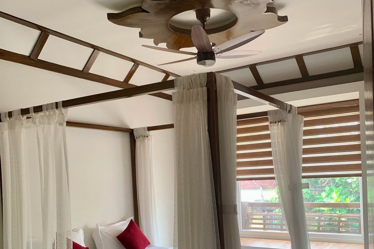 Una habitación con una cama, cortinas blancas, un ventilador de techo y baldosas de suelo con diseños.