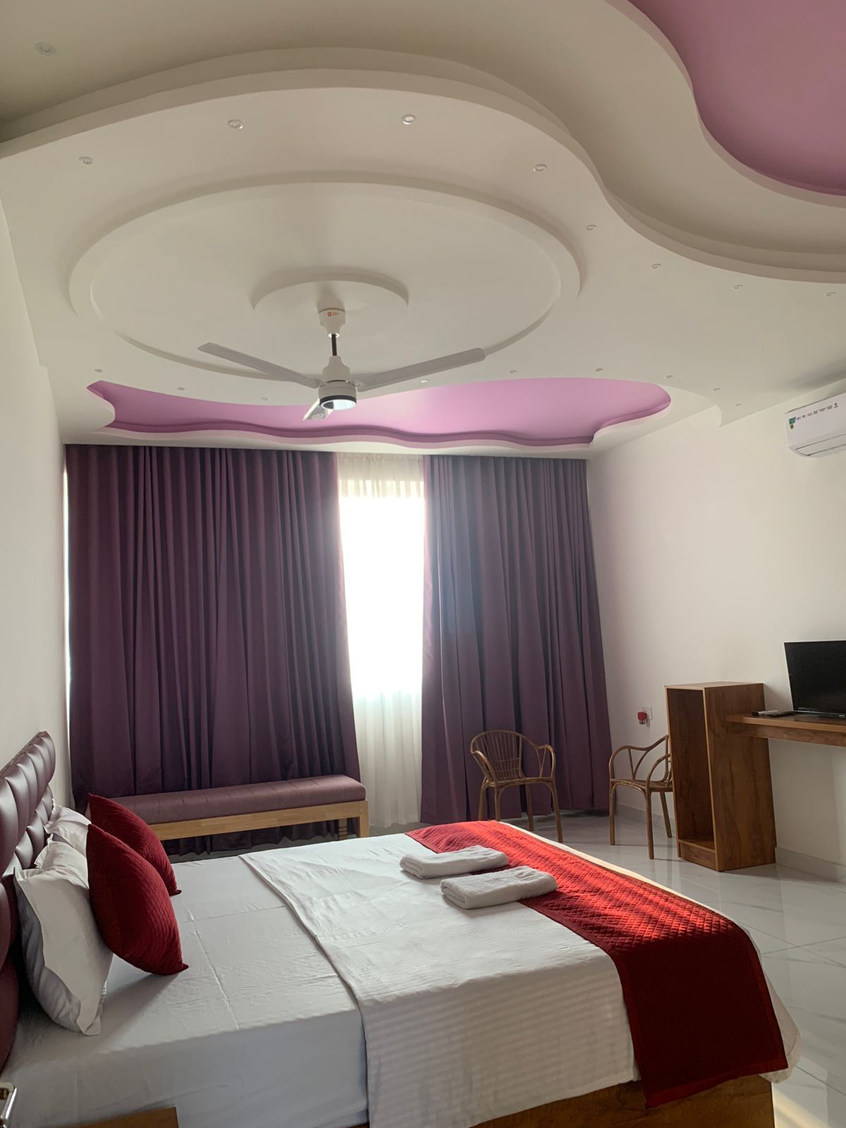 Hotellihuone, jossa on sänky, työpöytä, tuoli ja kattotuuletin.
