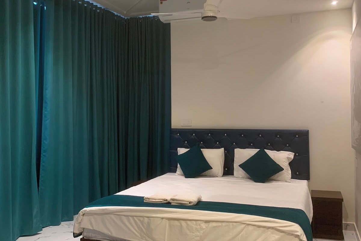 Una habitación de hotel moderna con una cama grande, cabecera oscura y cortinas color turquesa.