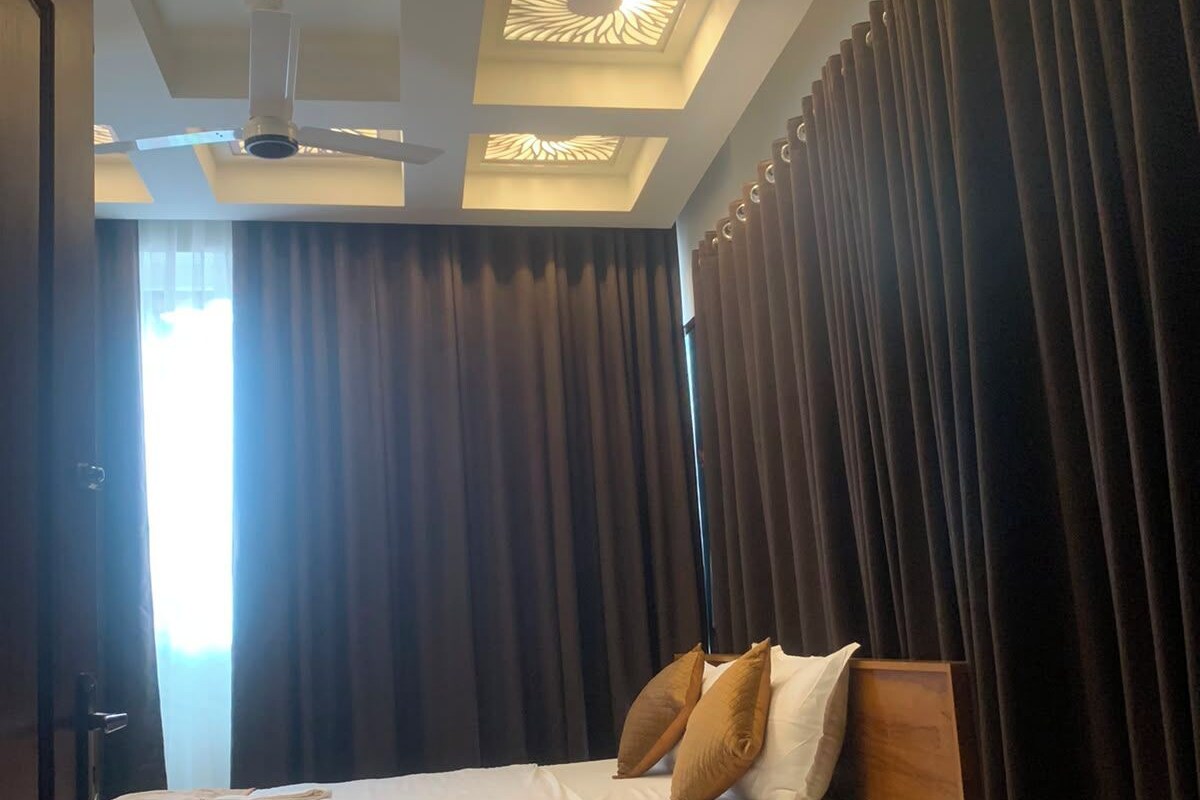 Una habitación de hotel con cama, cortinas, ventilador de techo y ventana con cortinas.