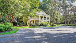 A two-story house with a porch, surrounded by lush greenery and trees. - Pawleys Island Golf + Beach Getaway w/ Pool Access (Pawleys Island)