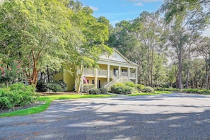 A two-story house with a porch, surrounded by lush greenery and trees. - Pawleys Island Golf + Beach Getaway w/ Pool Access (Pawleys Island)