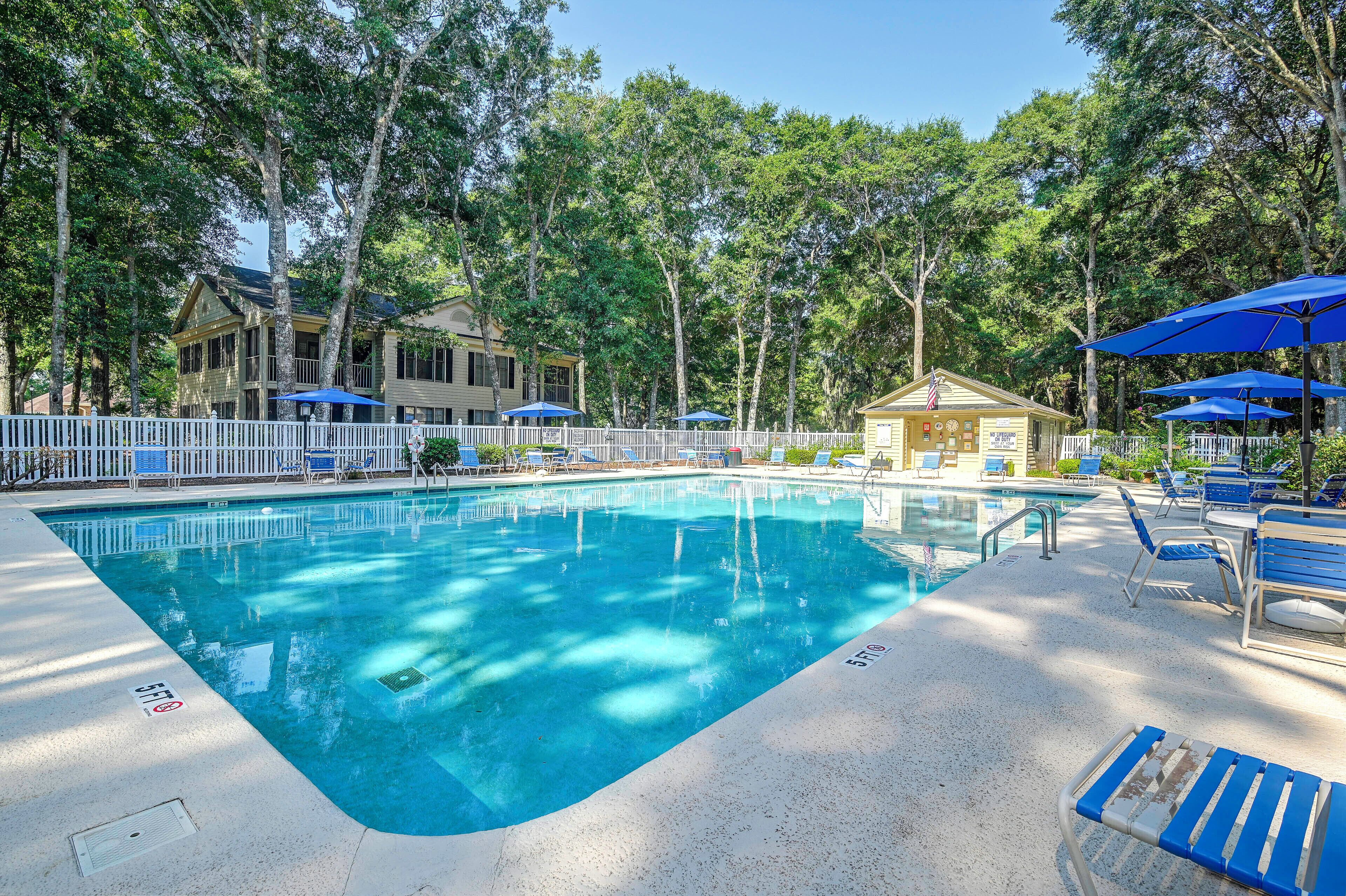 A swimming pool with lounge chairs and umbrellas, surrounded by trees and a building.