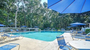 A pool area with lounge chairs and umbrellas, surrounded by trees. - Pawleys Island Golf + Beach Getaway w/ Pool Access (Pawleys Island)
