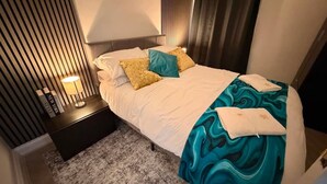 A hotel room with a bed, a nightstand, a lamp, and a window with curtains. - Stylish 3BR House in Newham East London (Greater London)
