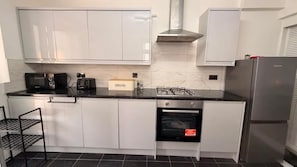 A modern kitchen with white cabinets, a black countertop, a built-in oven, and a stainless steel range hood. - Stylish 3BR House in Newham East London (Greater London)