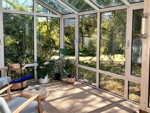 A conservatory with a glass roof, wicker furniture, and potted plants.