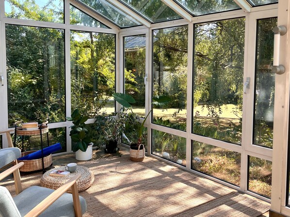 Un invernadero con techo de vidrio, mobiliario de mimbre y plantas en macetas.