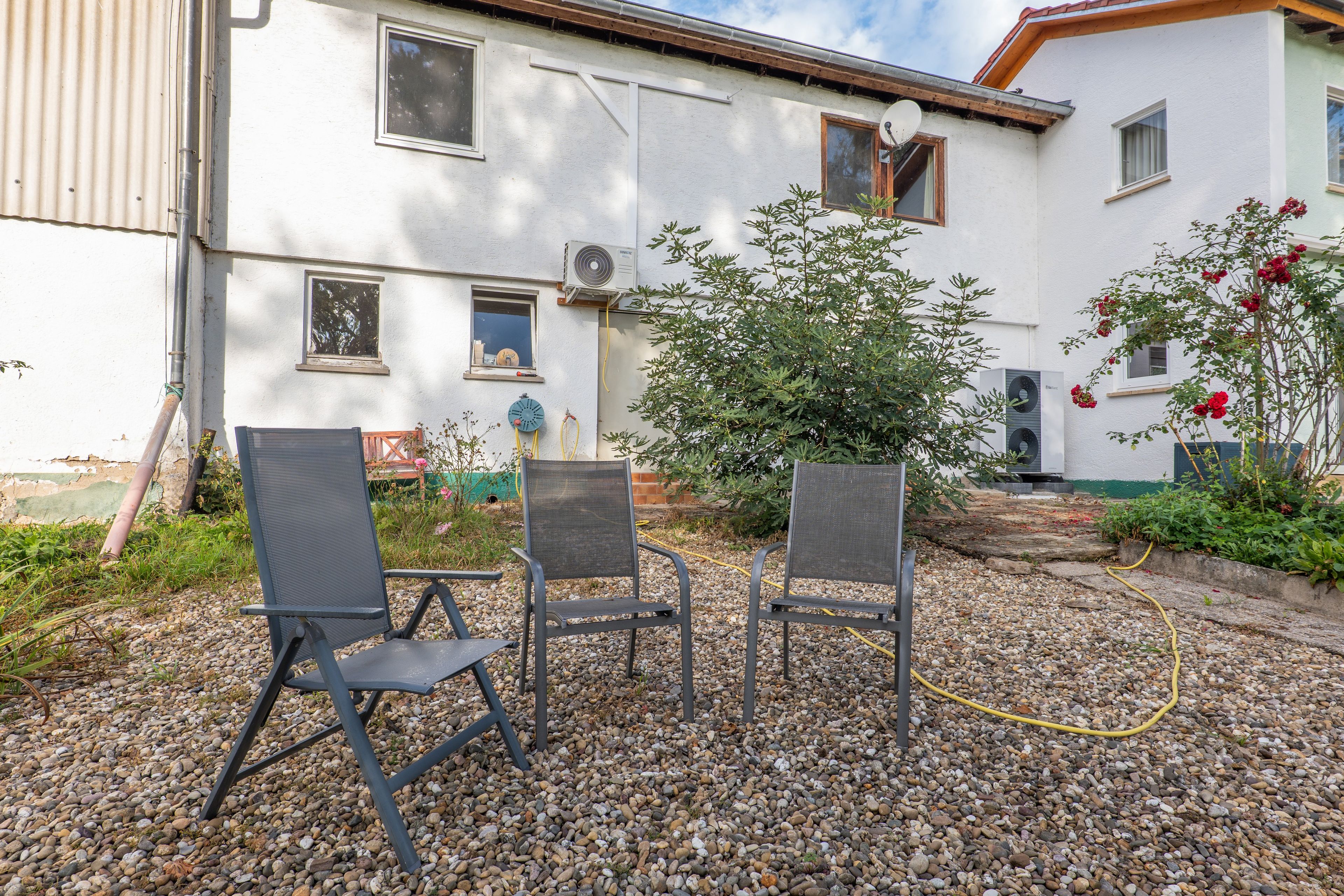An outdoor seating area with two chairs and a table, surrounded by a gravel patio and a white building with multiple windows.