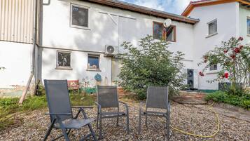 An outdoor seating area with two chairs and a table, surrounded by a gravel patio and a white building with multiple windows.