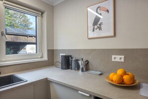 A kitchen with a window, a coffee maker, a kettle, and a plate of oranges.