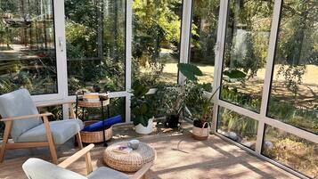 A conservatory with a glass ceiling, wooden furniture, and potted plants.