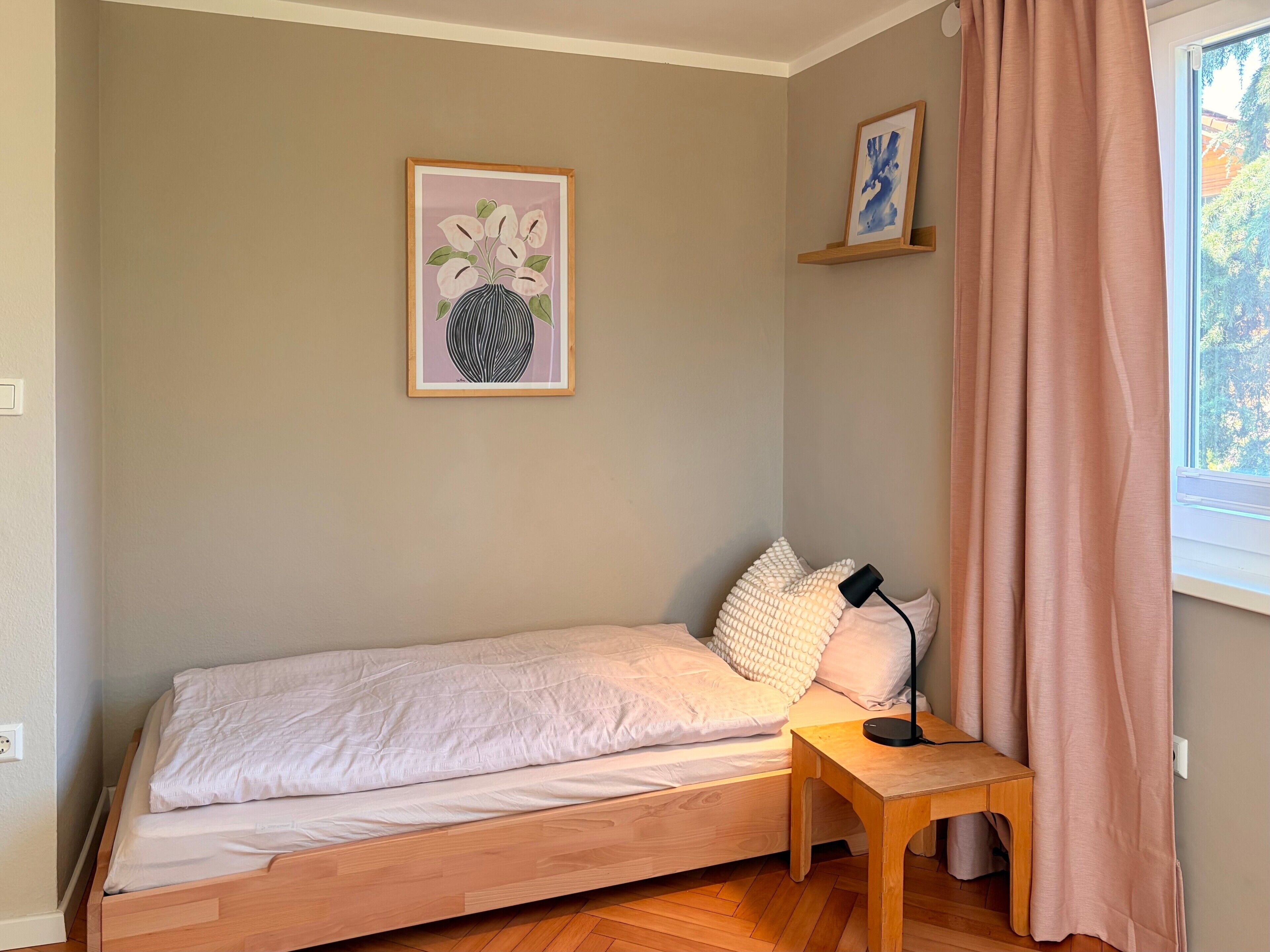 Un lit simple avec un cadre en bois, une table de chevet avec une lampe et une fenêtre avec des rideaux.