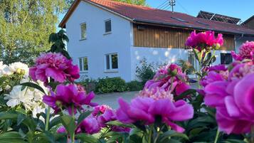 A white building with a red roof, surrounded by lush greenery and vibrant flowers.