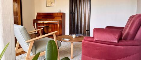 A living room with a piano, a red sofa, a coffee table, and a chair.