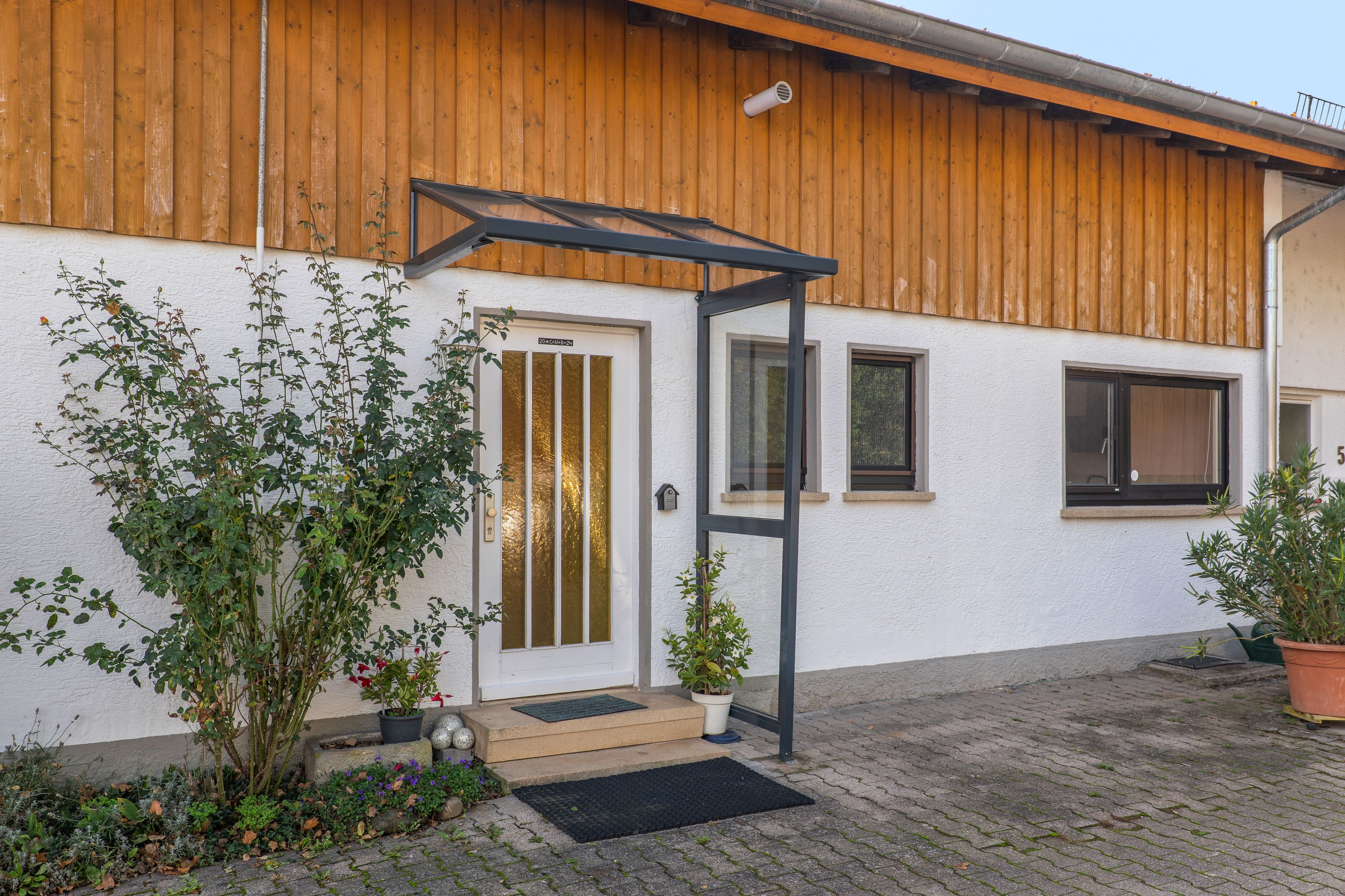 Ein modernes Gebäude mit einer Holzfassade, einer Glastür und einem kleinen Vorbau mit Metallrahmen.