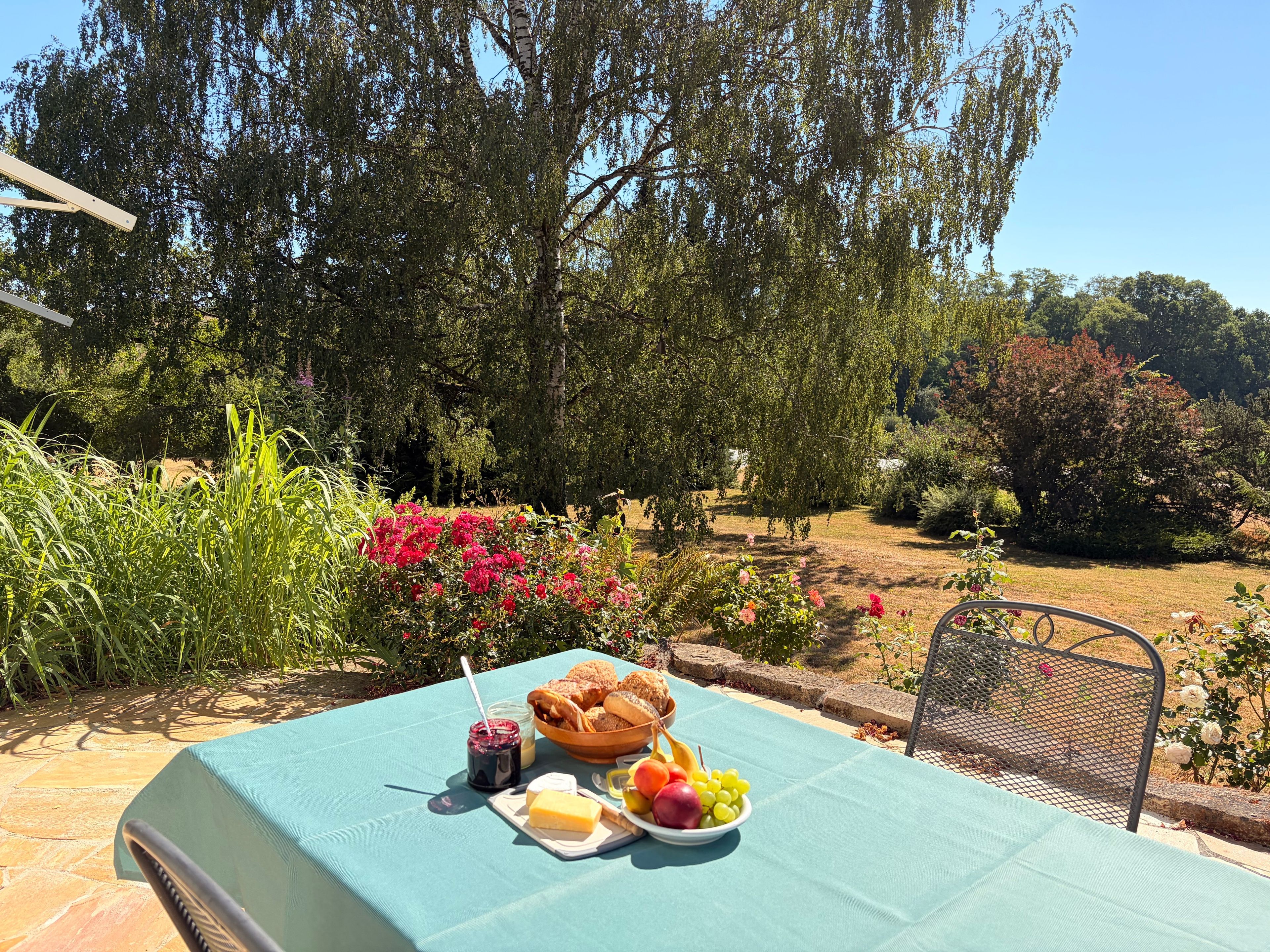 An outdoor dining area with a table set for a meal, surrounded by lush greenery and trees.