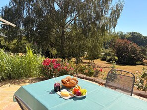 Un área de comedor al aire libre con una mesa lista para una comida, rodeada de abundante follaje y árboles.