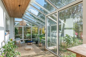 A conservatory with a wooden ceiling, large glass windows, and a seating area with a table and chairs.