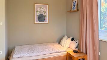 Un letto singolo con struttura in legno, un comodino con lampada e una finestra con tende.