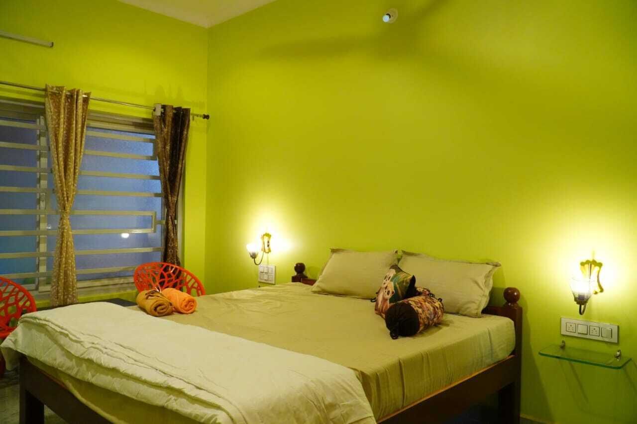 A room with a bed, two wall-mounted lamps, a window with curtains, and a small table with a lamp.