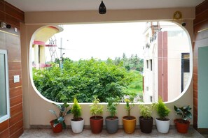 Una habitación con un ventanal grande, plantas en macetas y vistas al verdor exterior.